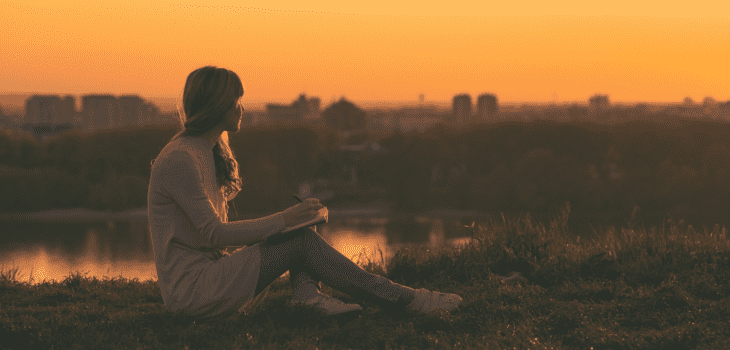 A woman watches a sunset and writes in her notebook