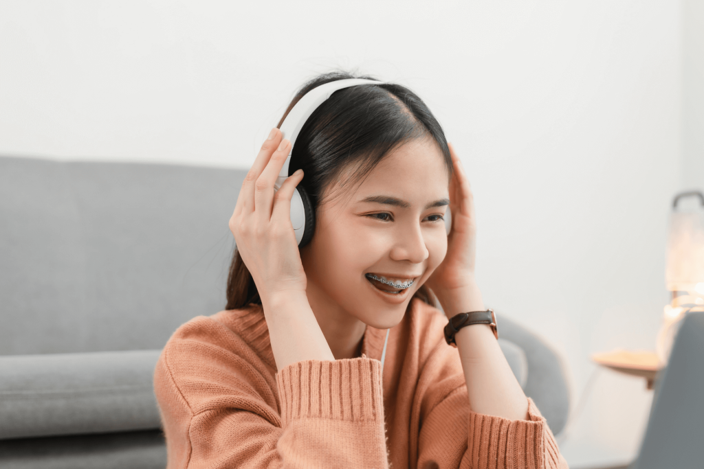 A girl in a sweater holding her headset as she listens to social audio app content.
