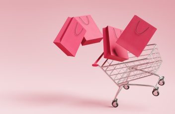 Four shopping bags and a shopping cart against a pink background