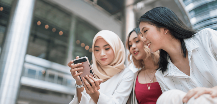 Three women looking at a phone while social media shopping